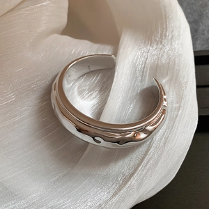 Gros plan d'un bracelet manchette argenté à texture de lave sur fond de soie blanche