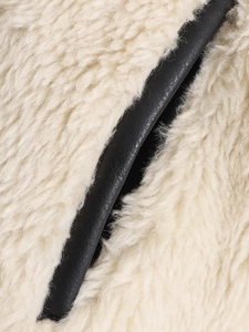Close-up of soft beige faux fur texture with black leather trim detail on jacket