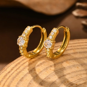 Detailed macro view of gold hoop earrings with pavé-set white zircon stones on wood