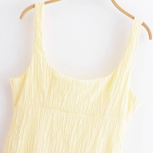 Pale yellow slip dress with vertical tree-bark texture hanging on a wooden hanger