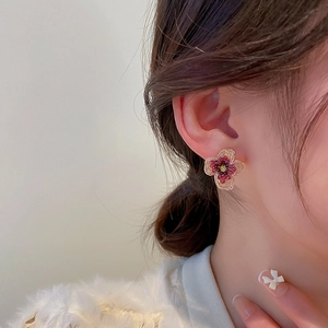 Close-up of deep red crystal flower stud earrings with elegant gold trim on model