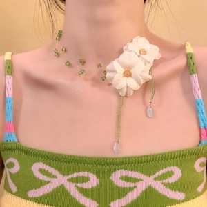 Primo piano di una collana floreale in tessuto con perline verdi e gocce d'acqua in vetro.