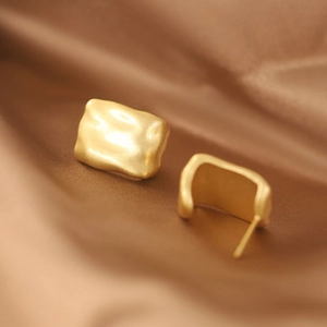 Macro shot of matte gold irregular rectangular stud earrings on silk fabric background