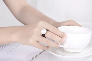 Detail of a minimalist black ring with a large white pearl on a model's finger