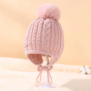Detail of pink knit baby hat featuring cable pattern, large pompom and ear flaps