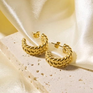 Detailed view of gold twisted rope hoop earrings on natural stone and silk fabric