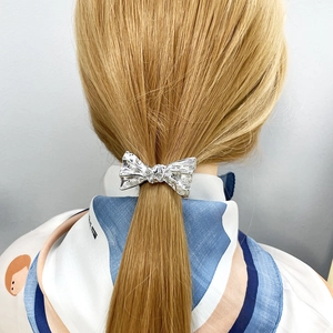 Minimalist silver bow metal hair clip shown on a low ponytail with a sleek finish
