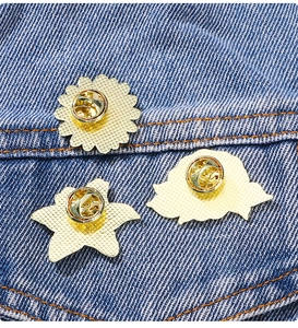 Detail of flower enamel brooches showing golden alloy back and butterfly clasp on denim
