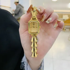 Dettaglio di un orologio dorato da donna con cassa rettangolare e cinturino geometrico