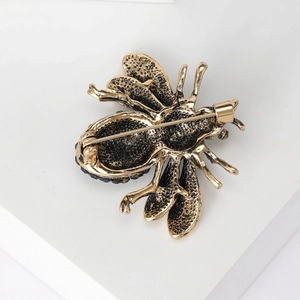 Vintage bronze bee brooch with rhinestones shown on a white geometric stand