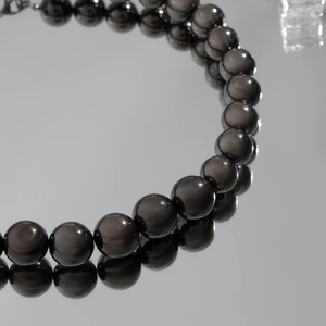 Close-up of polished dark grey CCB round beads on a reflective surface for hip-hop necklace
