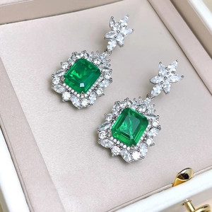 Elegant emerald cut green drop earrings with halo diamond setting in a jewelry box