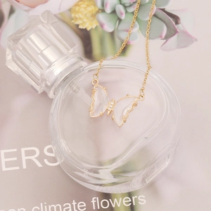 Close-up of golden butterfly necklace with transparent resin wings on a glass bottle
