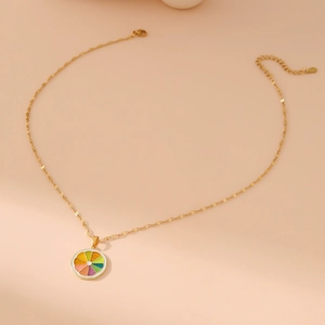 Golden necklace with colorful citrus slice pendant on a minimalist beige background