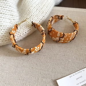 Détail de créoles en tissu orange avec imprimé paisley bohème sur fond de maille douce