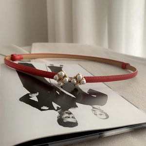 Detailed shot of a red leather belt featuring a refined pearl flower buckle on a magazine