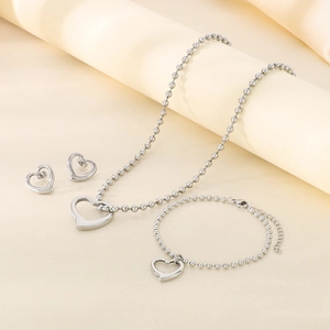 Detailed set of silver hollow heart pendant necklace, bracelet, and stud earrings on fabric