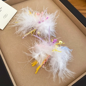 Detailed macro view of fluffy white feather earrings with colorful accents on jewelry tray