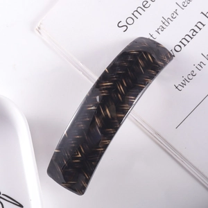 Close-up of a dark brown acetate hair clip with herringbone pattern on a book and plate