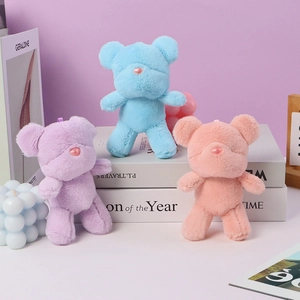 Three colorful candy-colored plush bear keychains on books in a cozy setting