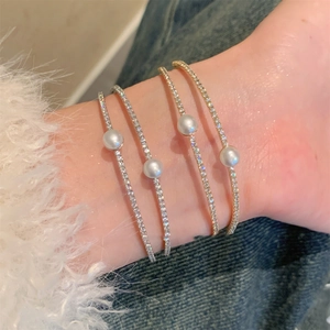Close-up of stacked zircon pearl bracelets in gold and silver finish on a wrist