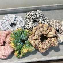 Detailed view of tweed fabric hair ties in various colors on a soft grey display tray