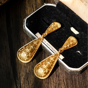 Detailed view of gold leaf-shaped earrings with swirl patterns on a velvet box