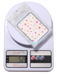Floral nail stickers in packaging weighed on a scale showing a total mass of 5.2 grams