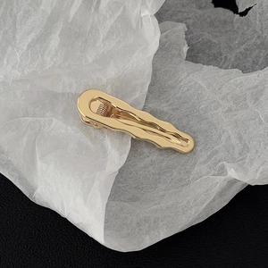 Close-up of golden irregular wave edge metal hair clip with polished finish