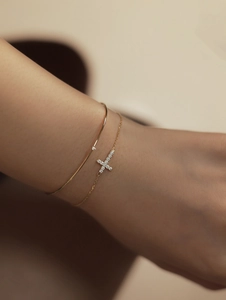 Close-up of a delicate 18K gold-plated cross bracelet with sparkling zircon on a wrist