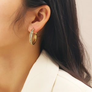 Close-up of a gold hoop earring with pavé zircon stones worn on an ear for a luxury look