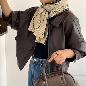 Detail of a beige knit scarf with geometric patterns paired with a brown leather jacket