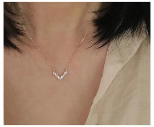 Close-up of V-shaped gold pendant with baguette-cut zircon stones on a female model