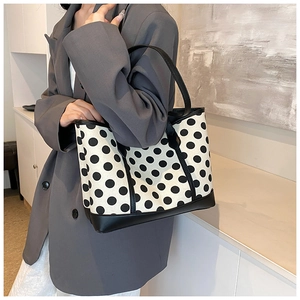 Polka dot tote bag with black leather handles held by a model in a gray blazer
