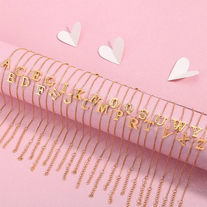 Gold letter necklace with sparkling crystals on a textured pink background