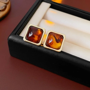 Close-up of square amber resin stud earrings with golden metal frame in a black jewelry box