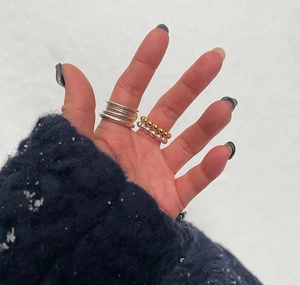 Detail of silver multi-layer coil and bead rings worn with a blue knit sweater