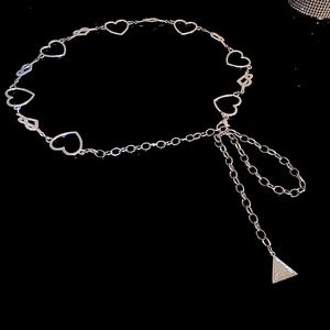 Silver metal heart-shaped cutout chain belt with triangular pendant on black background