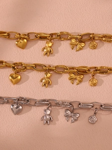 Detail of 18K gold plated chain bracelet with bear, heart and bow charms on pink texture
