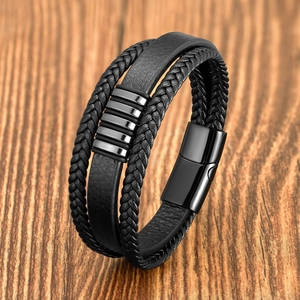 Detail of multi-layer braided black leather bracelet with metal magnetic clasp on wood
