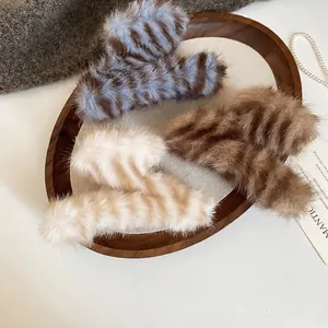 Trois pinces à cheveux en peluche rayée bleue, marron et beige sur un plateau en bois