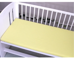 Detailed close-up of a vibrant yellow cotton crib sheet on a white wooden infant bed