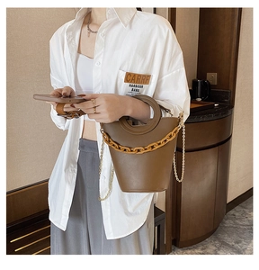 Detail view of a brown bucket bag with amber acrylic chain and metal strap on model