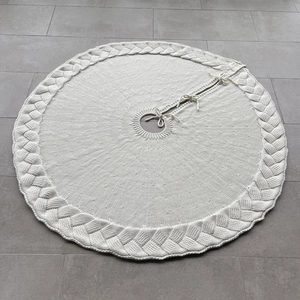 Detail of knitted cream white Christmas tree skirt with thick cable weave and ties