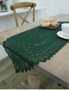 Close-up of dark green lace crochet table runner with delicate scalloped edges on wood