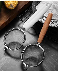 Close-up of fine stainless steel mesh strainers with wooden and white handles in kitchen