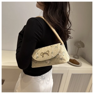 Détail de la broderie florale et du nœud doré sur un sac porté épaule en paille beige