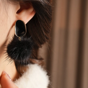 Close-up of black fuzzy pom pom earrings with oval enamel detail worn on model