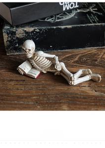 Detailed view of skull figurine reading a red book on a rustic wooden desk