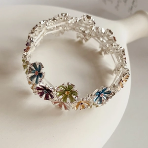 Macro shot of silver flower bracelet with colorful enamel details on white surface
